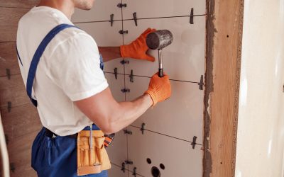 Male worker installing ceramic wall tile in house Close up of young man construction worker using rubber hammer while placing tile on the wall
